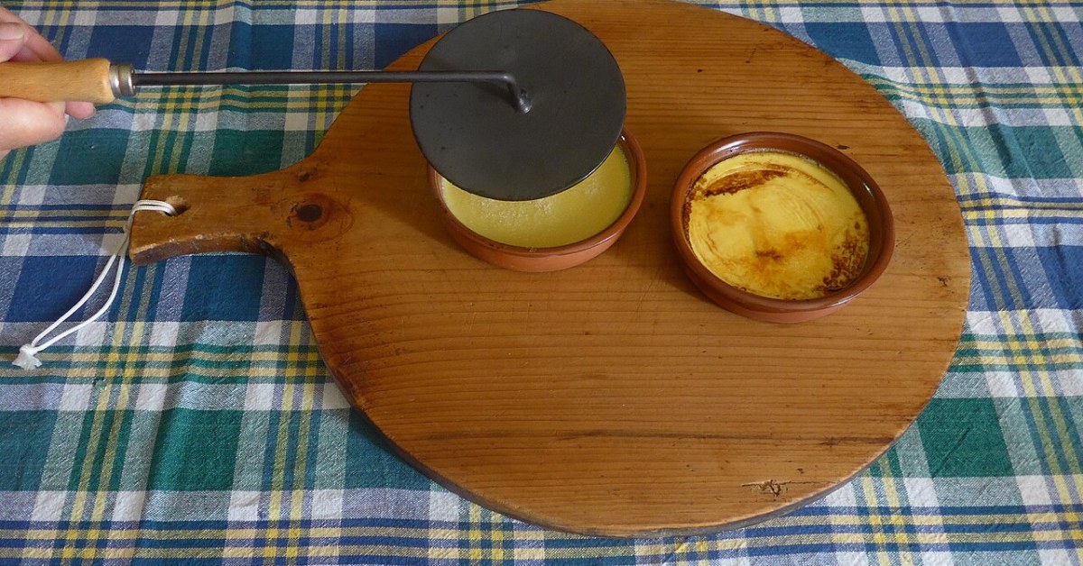 Disque de fonte chauffé au feu posé sur une crème aux œufs, à côté d'une crème déjà caramélisée